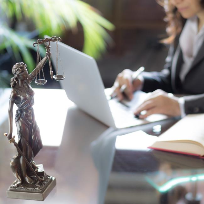 A lawyer in the eDiscovery process, working on her laptop with a justice scale statue on her desk.